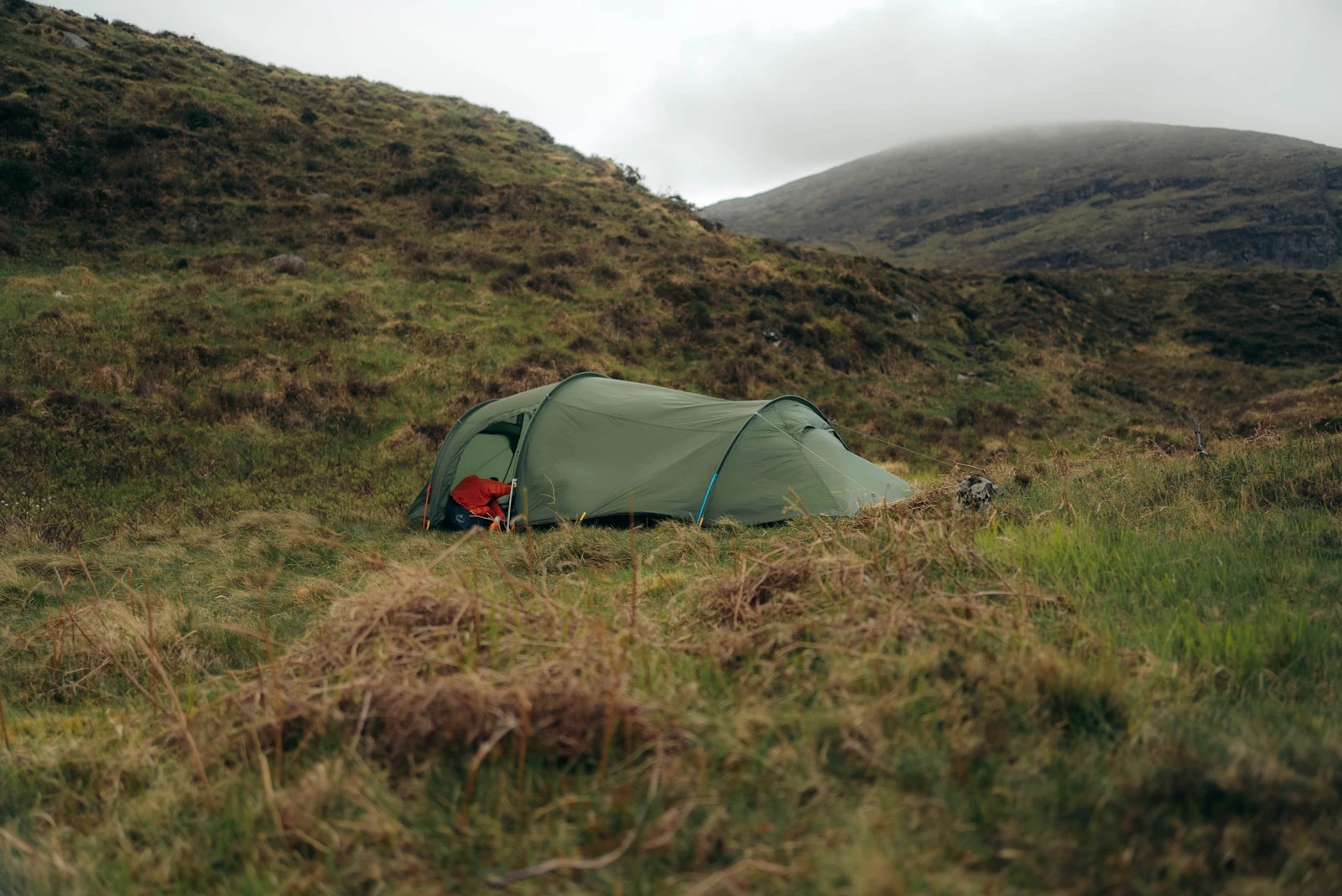A green tent pitched on a rough, misty hillside